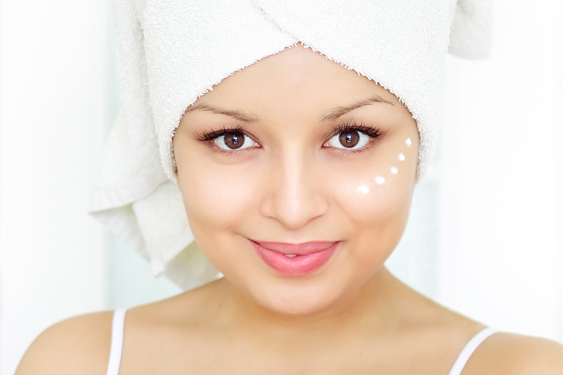 Girl applying cosmetic cream on skin on a light background in room